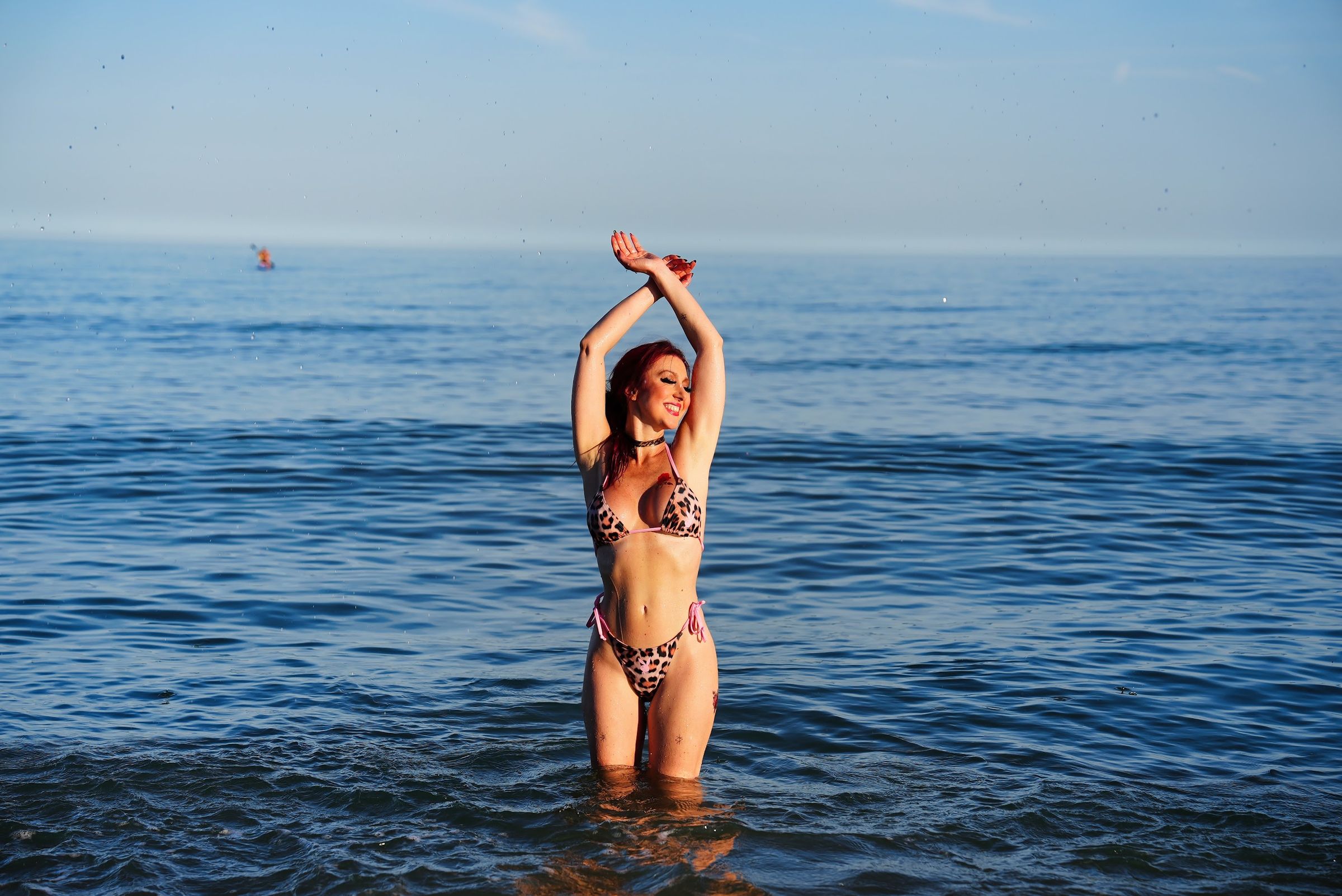 Yulia standing waist-deep in a calm blue sea with her arms raised above her head